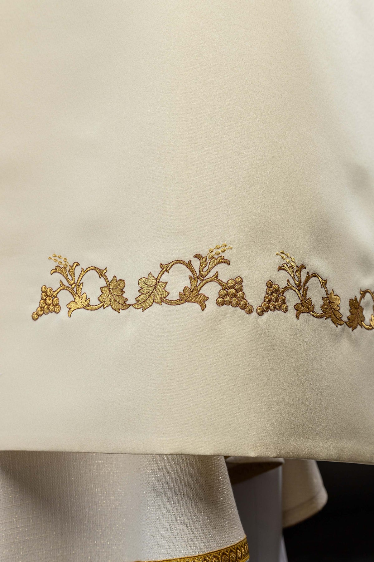 Velo humeral crudo en detalle, con bordado dorado de hojas y racimos de uvas