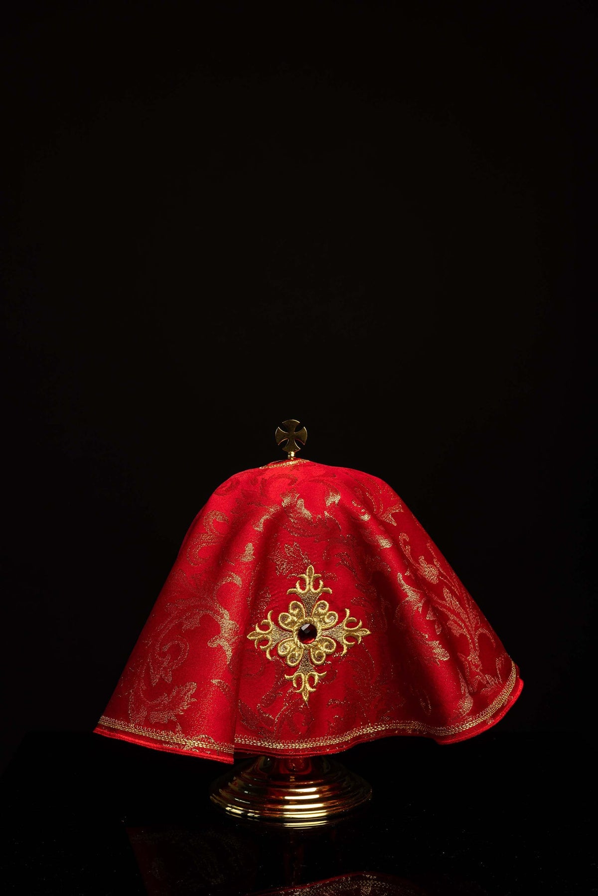 Cubrecopón redondo rojo con cruz bordada y piedra decorativa, vista frontal