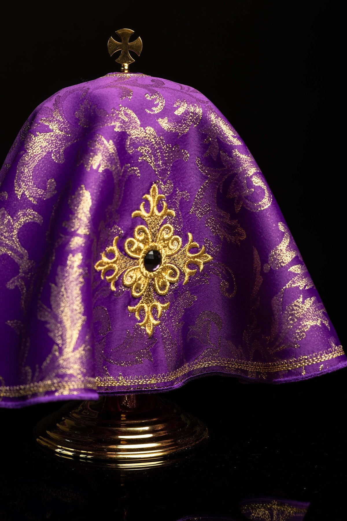 Cubrecopón morado con cruz bordada y piedra decorativa, vista frontal cercana